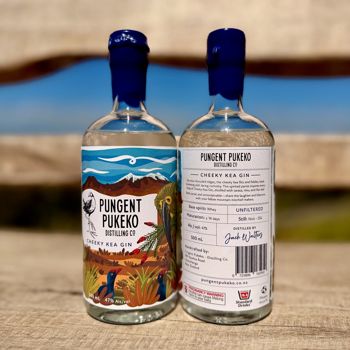 Two bottles of Pungent Pukeko Cheeky Kea Gin on a wooden surface with a blurred natural background.